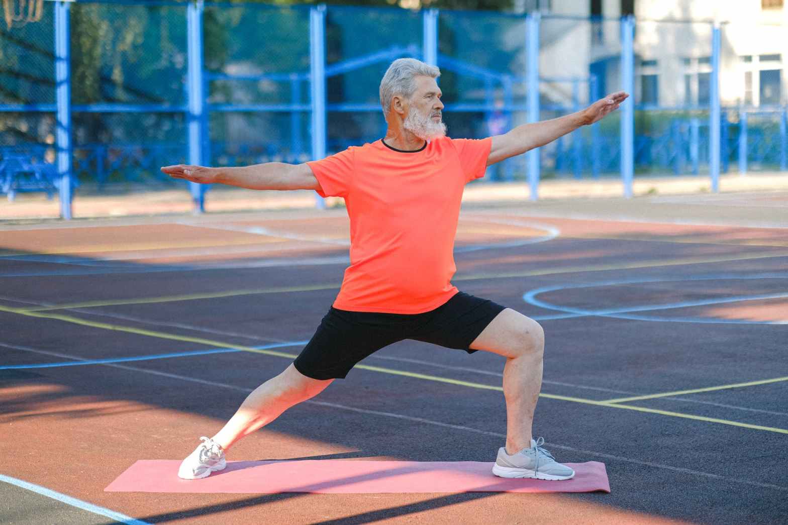 senior man in orange shirt and black pants doing yoga